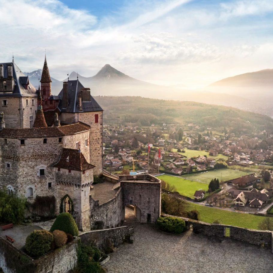 Château médiéval surplombant un paysage vallonné avec montagnes et villages.