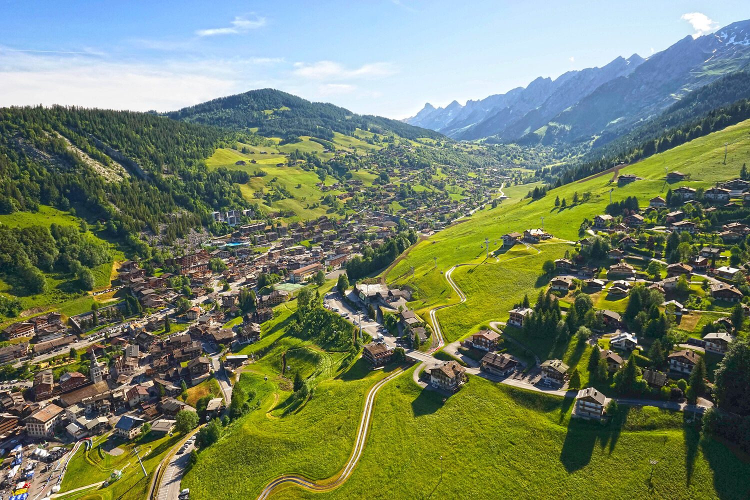 Circuit touristique Classe-Affaires VTC Paysage alpin verdoyant avec un village pittoresque et des montagnes en arrière-plan.