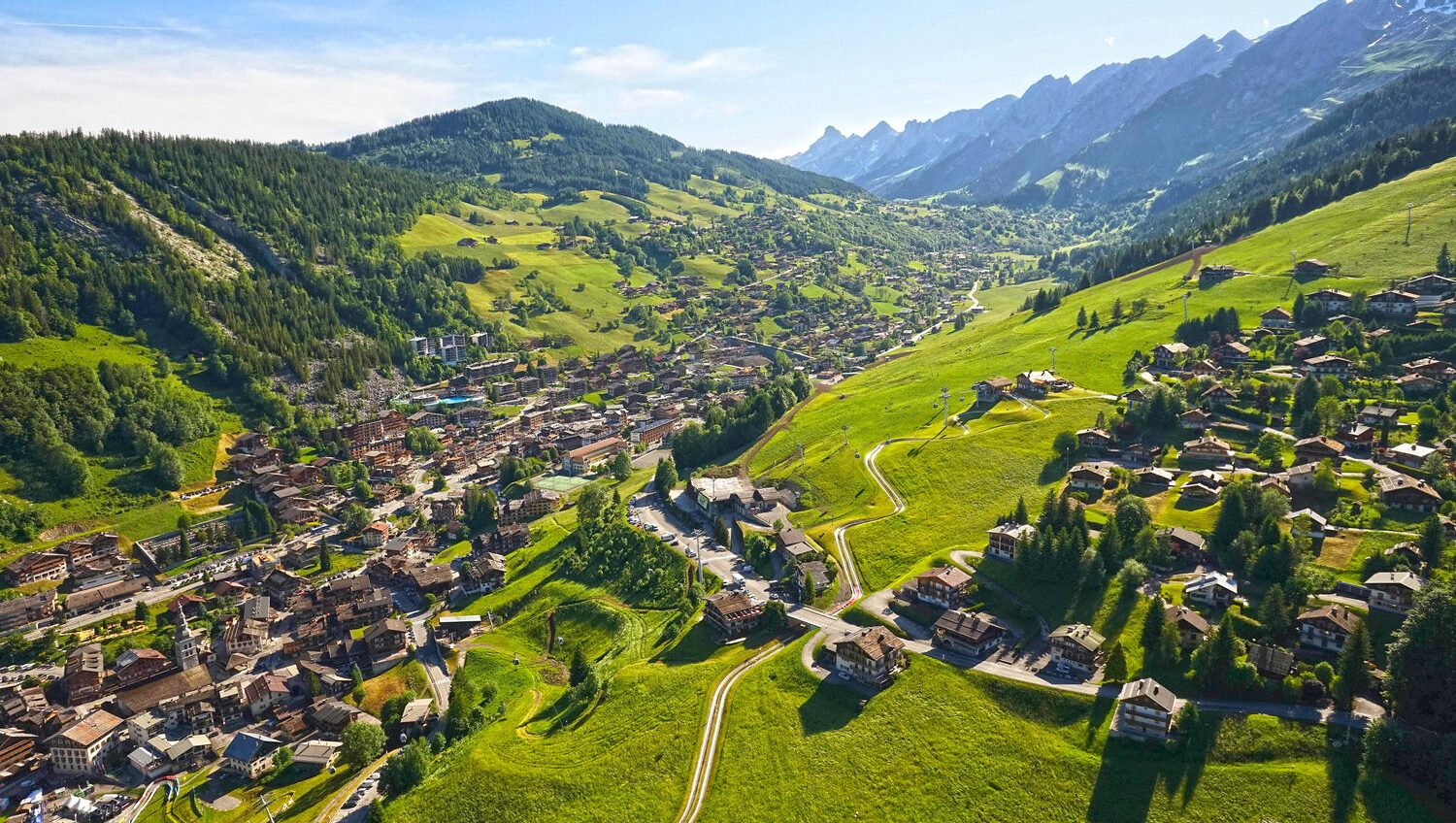 Classe-Affaires VTC - Chamonix Mont-Blanc Haute-Savoie Vue aérienne d'un village alpin des Aravis entouré de collines verdoyantes et de montagnes.