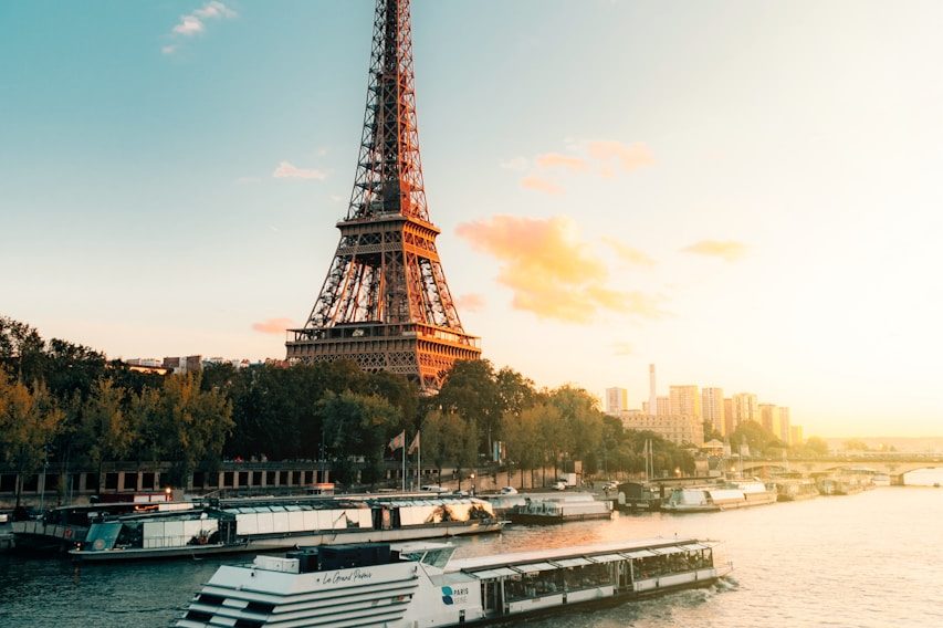 Tour Eiffel au coucher du soleil, avec des péniches sur la Seine en premier plan.
