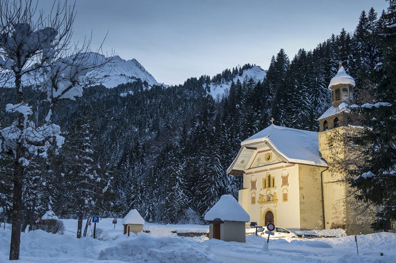 Notre Dame de la Gorge aux Contamines-Montjoie entouré de neige, avec montagnes en arrière-plan au crépuscule.