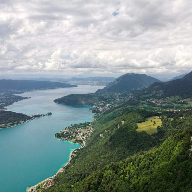 Vue panoramique du lac d'Annecy, entouré de montagnes et de nuages.