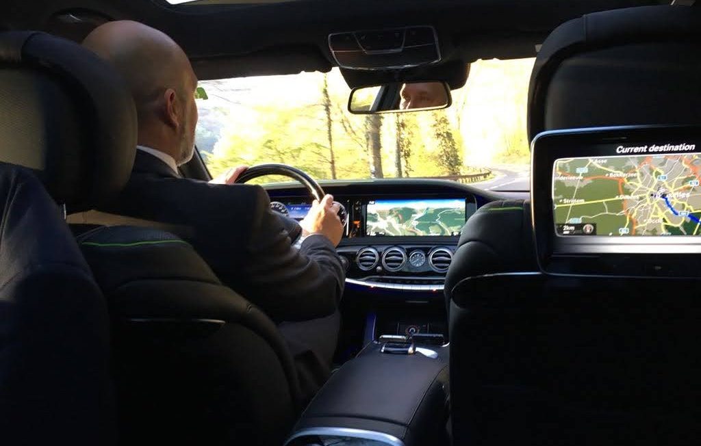 A driver's hand holding the steering wheel, seen through the blurred windshield.