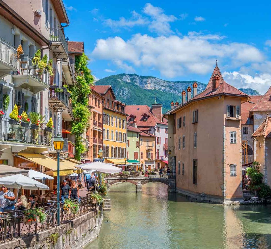 Classe-Affaires VTC Chamonix Mont-Blanc Annecy Canaux pittoresques d'Annecy, avec bâtiments colorés et montagnes en arrière-plan.
