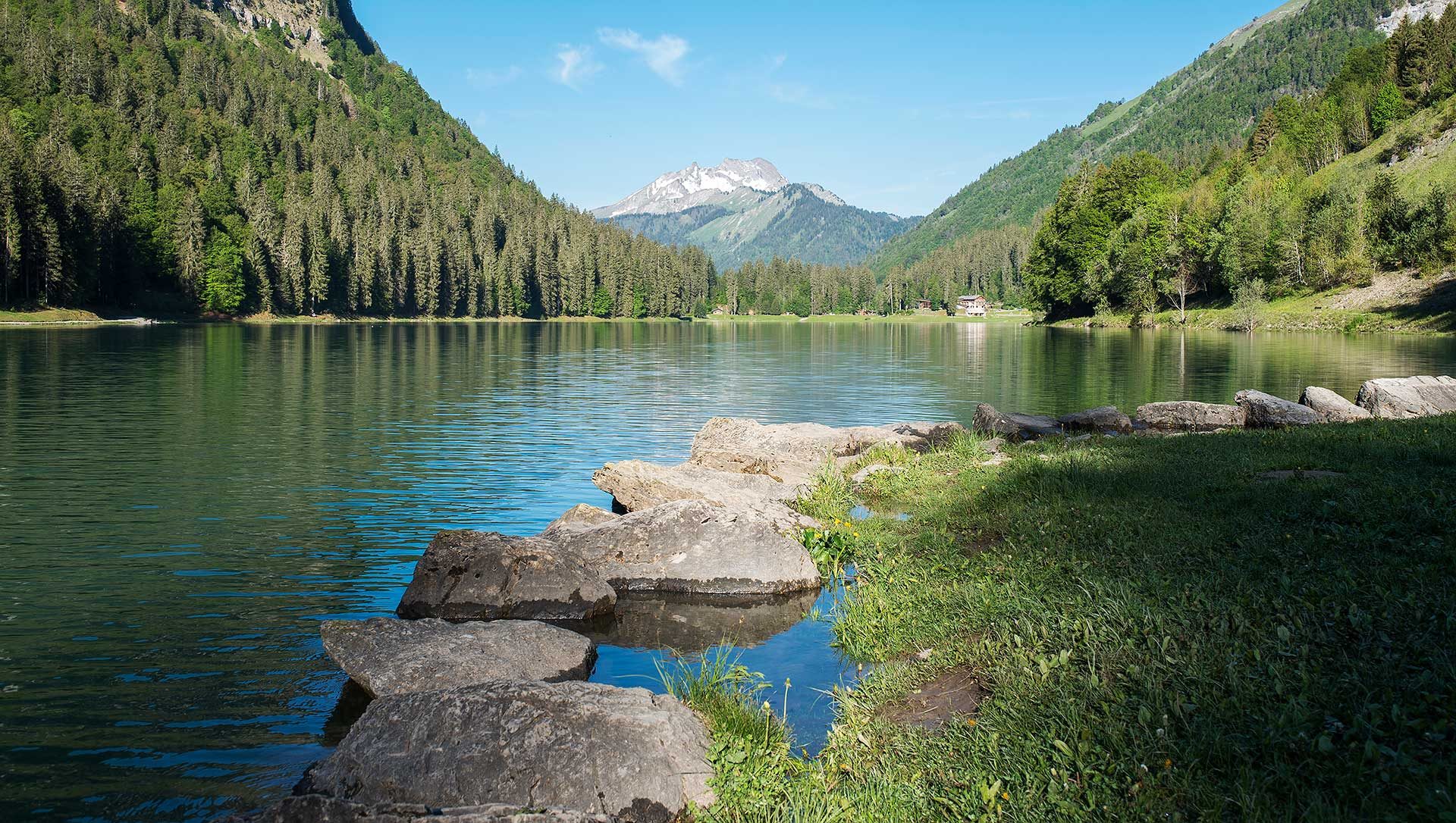 Classe-Affaires VTC - Chamonix Mont-Blanc Haute-Savoie Lac tranquille entouré de montagnes, avec des pierres au bord et verdure.