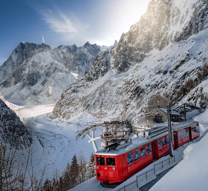Train rouge en montagne, entouré de neige, avec des sommets majestueux en arrière-plan.